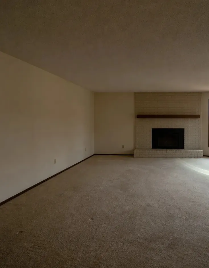 An empty living room as photographed: brick fireplace, bare floor